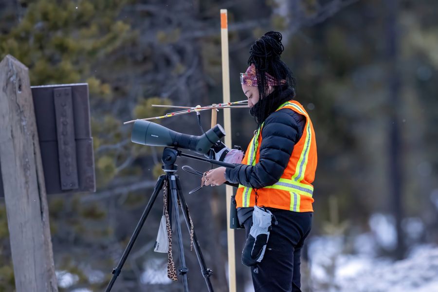 Taylor in a hi-vis vest at a spotting scope topped with a telemetry antenna, snow on the ground