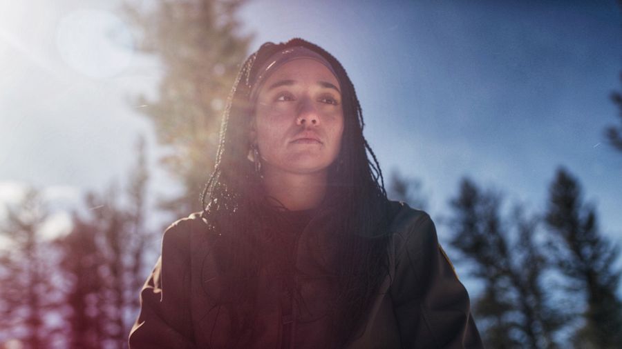 Taylor in the forest under a blue sky, the sun flaring across the lens